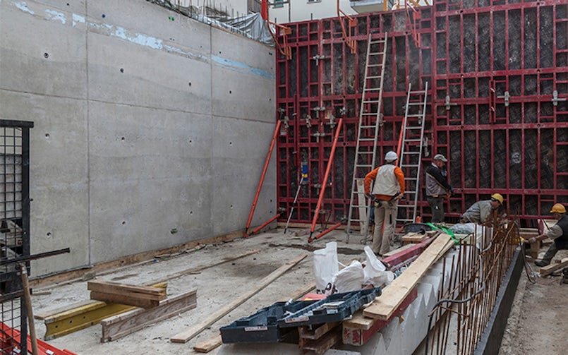 Overzicht van de bouwplaats tijdens het storten en uitharden van betonwanden, met nadruk op de ruwe betontoepassing